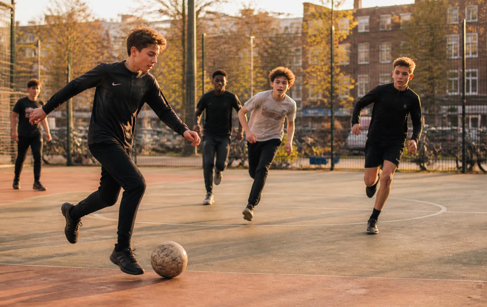 Jongens spelen samen een partijtje voetbal op een pleintje in de stad